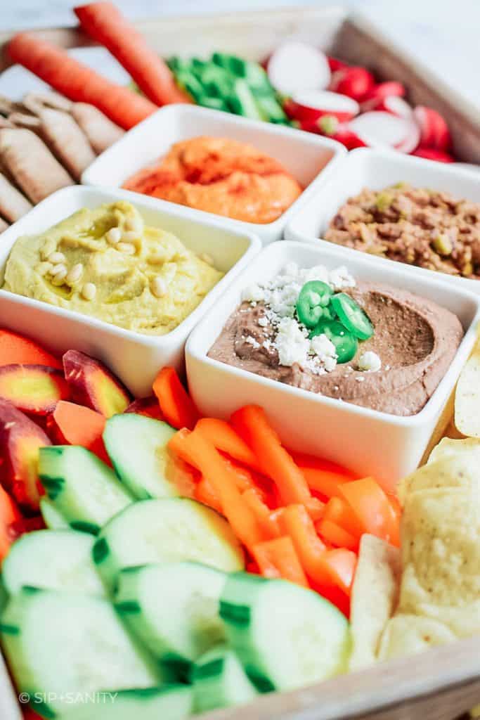 snack board with three kinds of hummus, veggies and chips