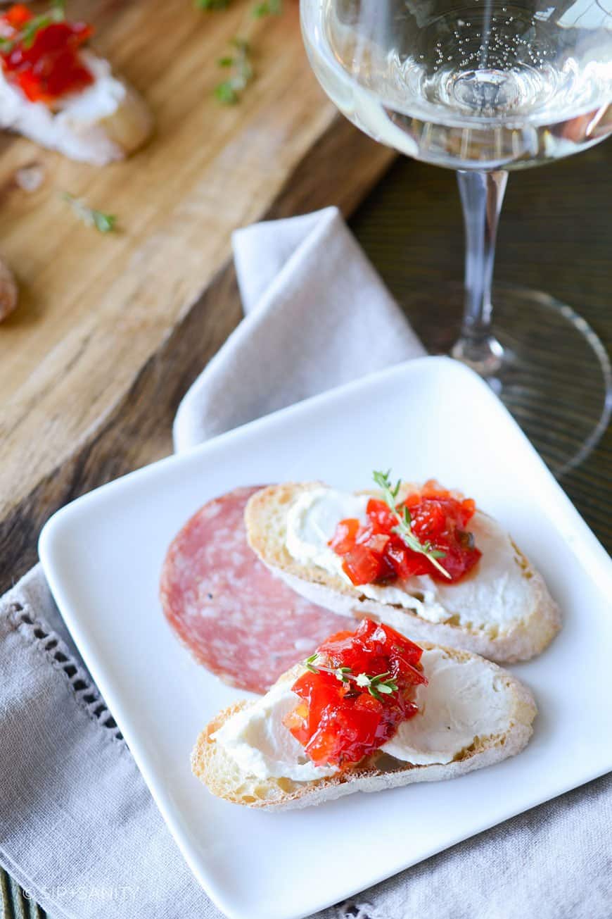 two crostini and salami on a plate and glass of white wine