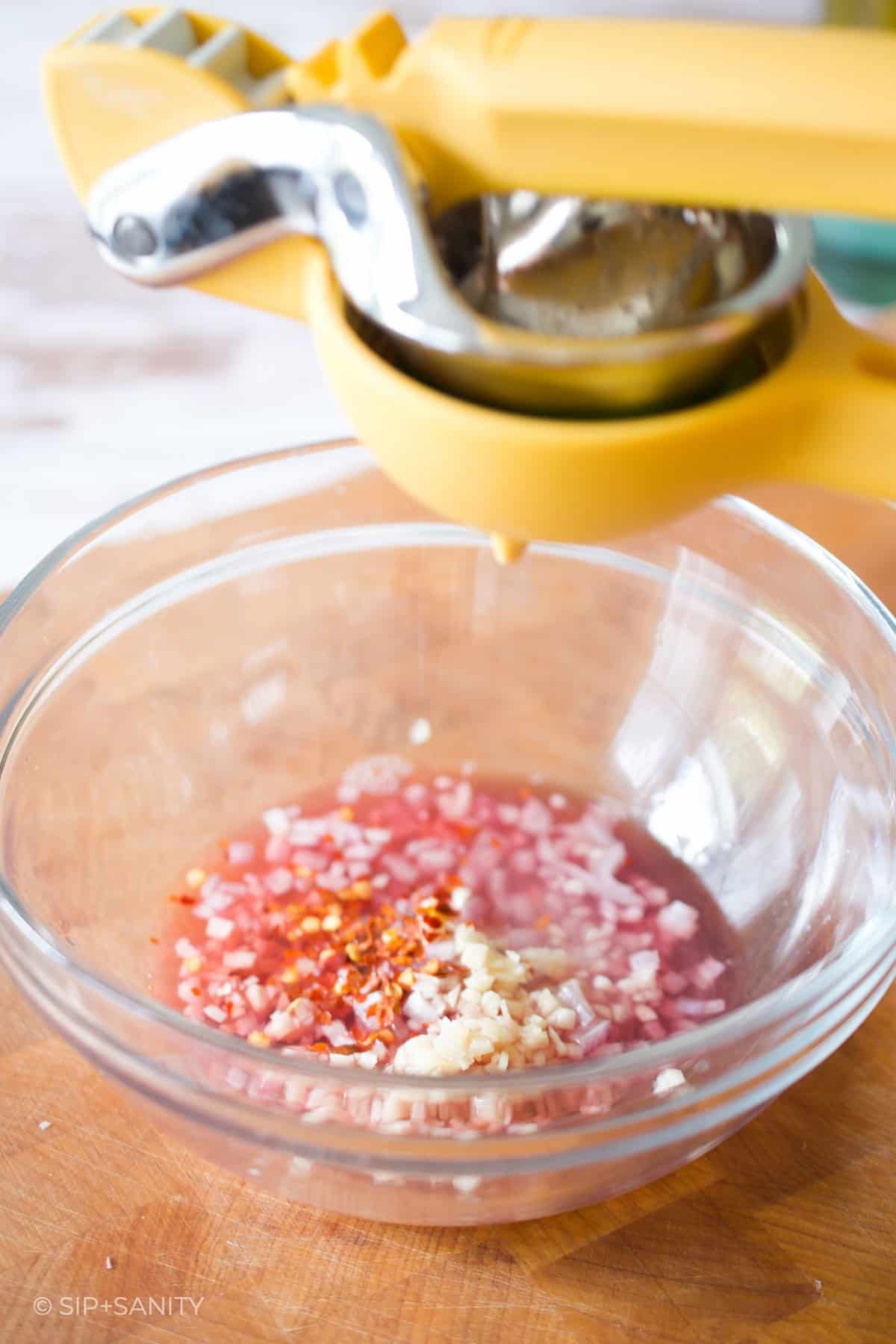 squeezing lime juice into a bowl with shallots and garlic