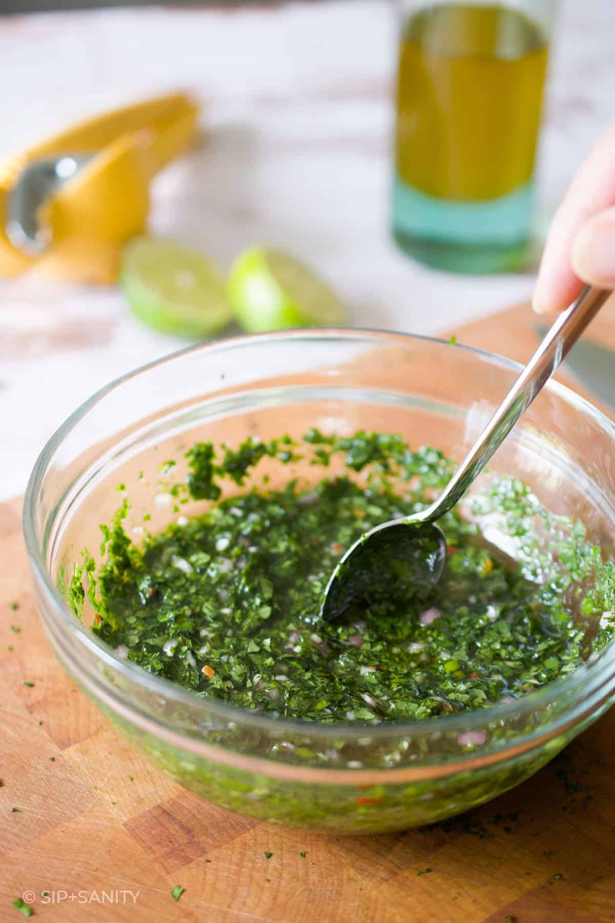 stirring a bowl of chimichurri sauce with a spoon