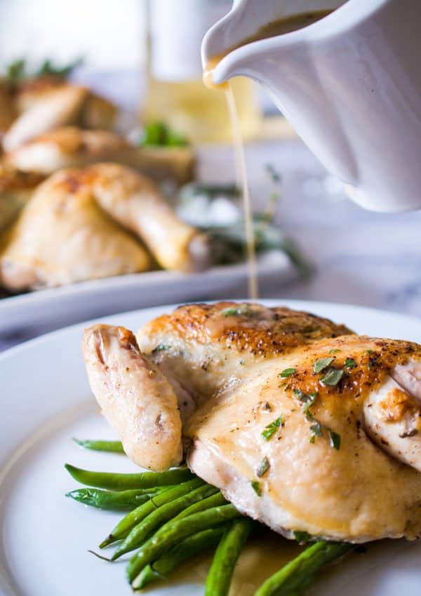 white wine pan sauce pouring over half a cornish hen