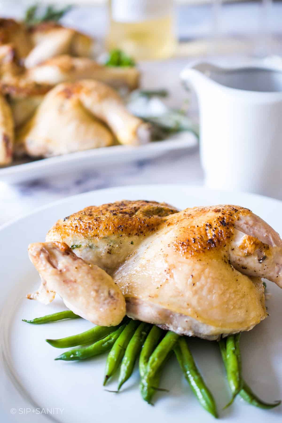half a roasted butterflied cornish hen and green beans on a plate