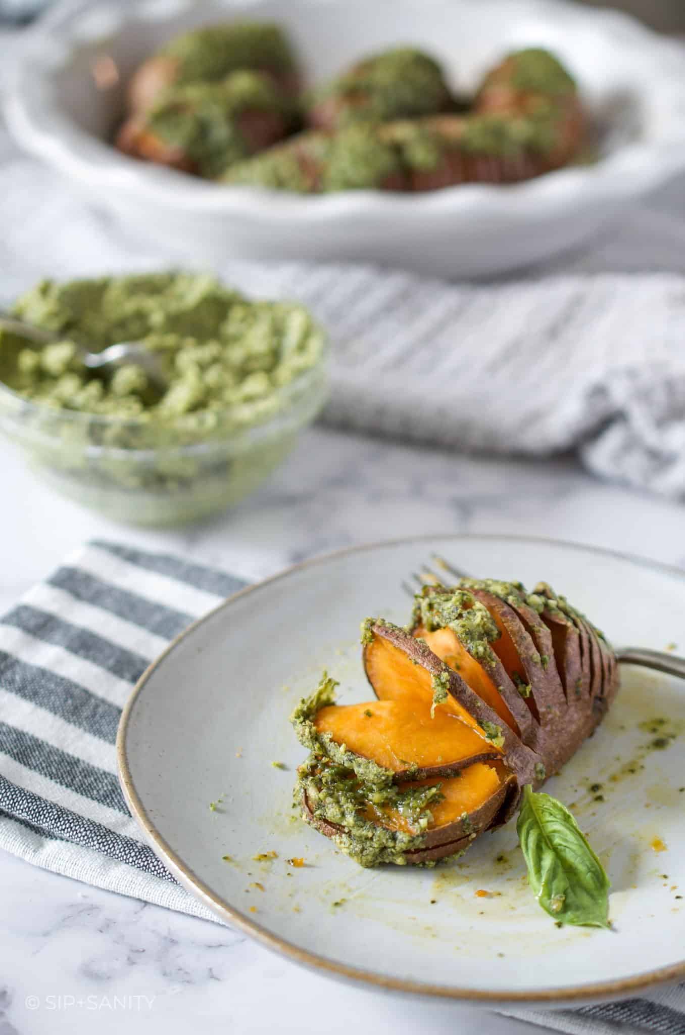 pie dish with roasted sweet potatoes, bowl of pumpkin seed pesto butter and single potato on a plate