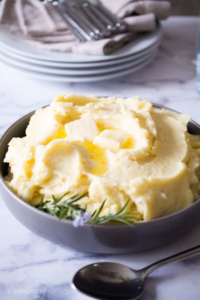bowl of roasted garlic mashed potatoes next to stack of plates