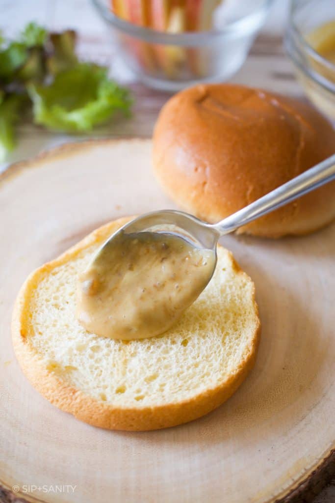 spreading dijonnaise on a toasted bun