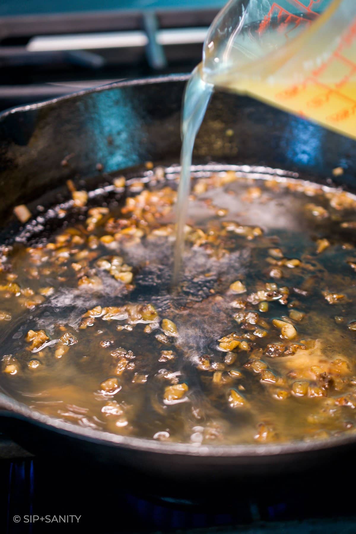 liquid being poured into a skillet with shallot and garlic