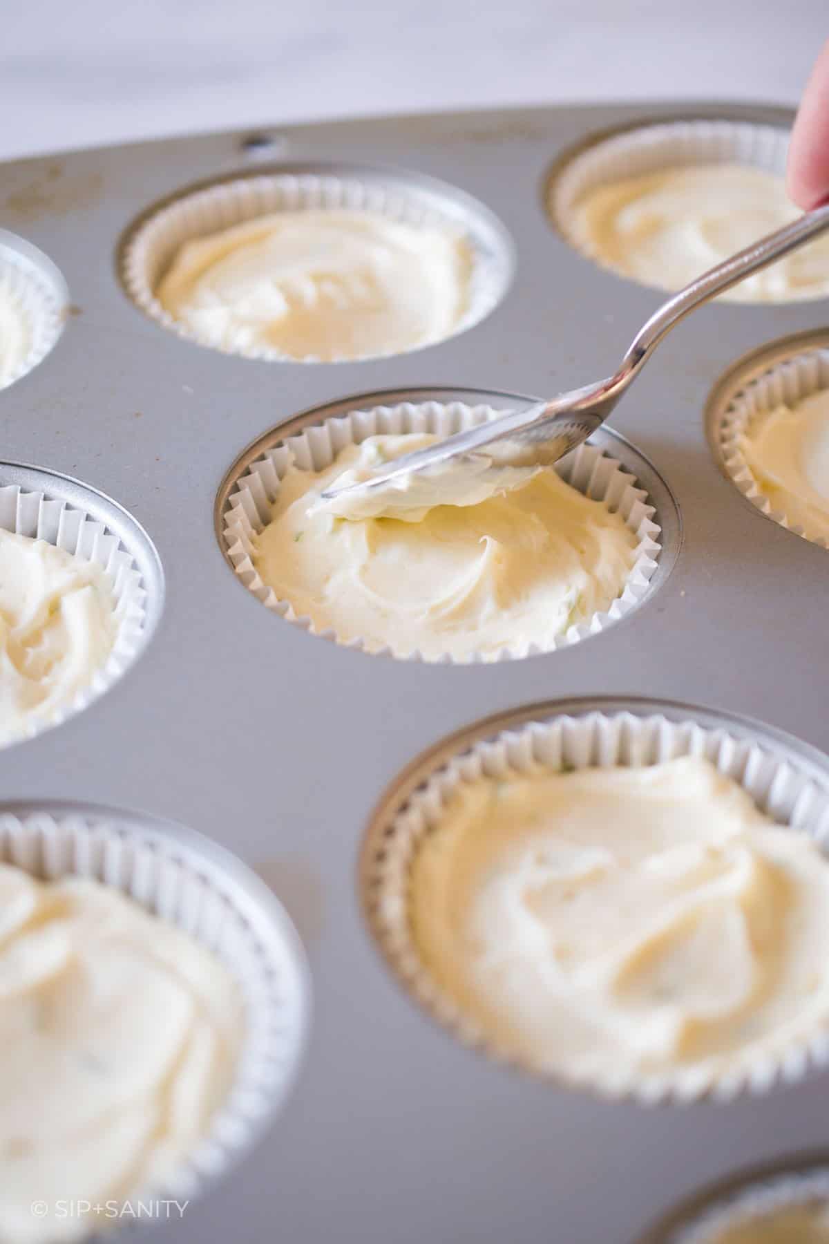 spreading cheesecake mix into muffin cups