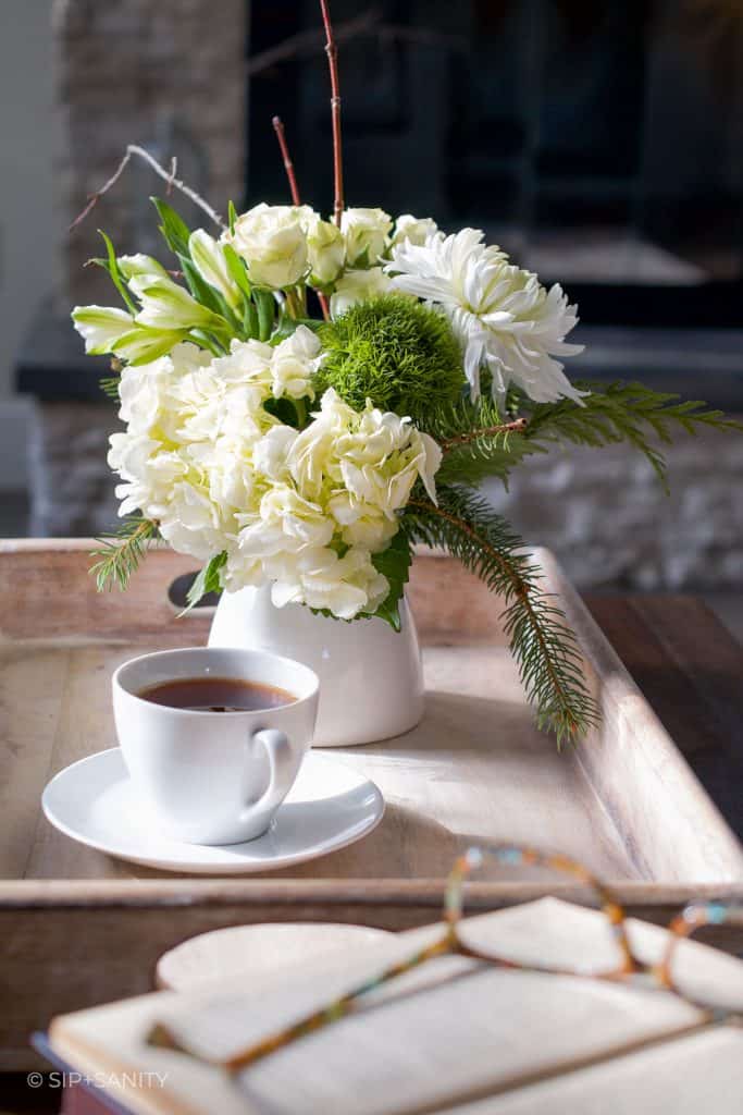 a cup of tea and vase of flowers on a tray.