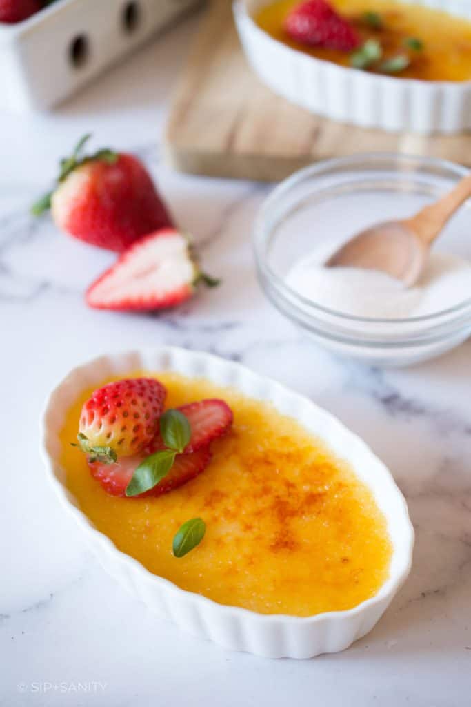 Basil creme brûlée with strawberries and a bowl of sugar.