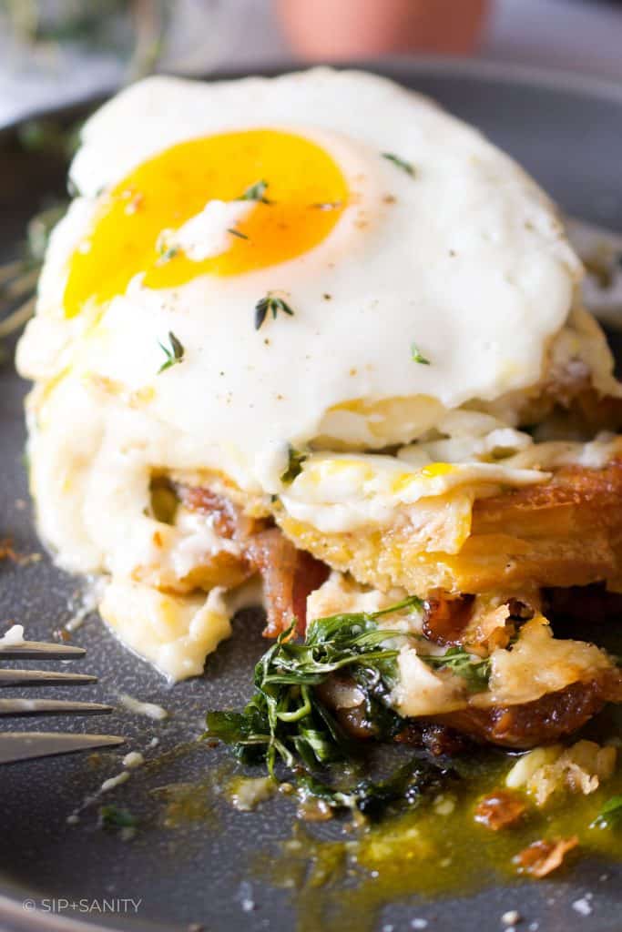 A cut open candied bacon and arugula croque madame on a plate with a fork.