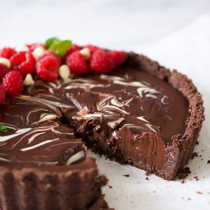 A chocolate tart with raspberries on top on a white background.
