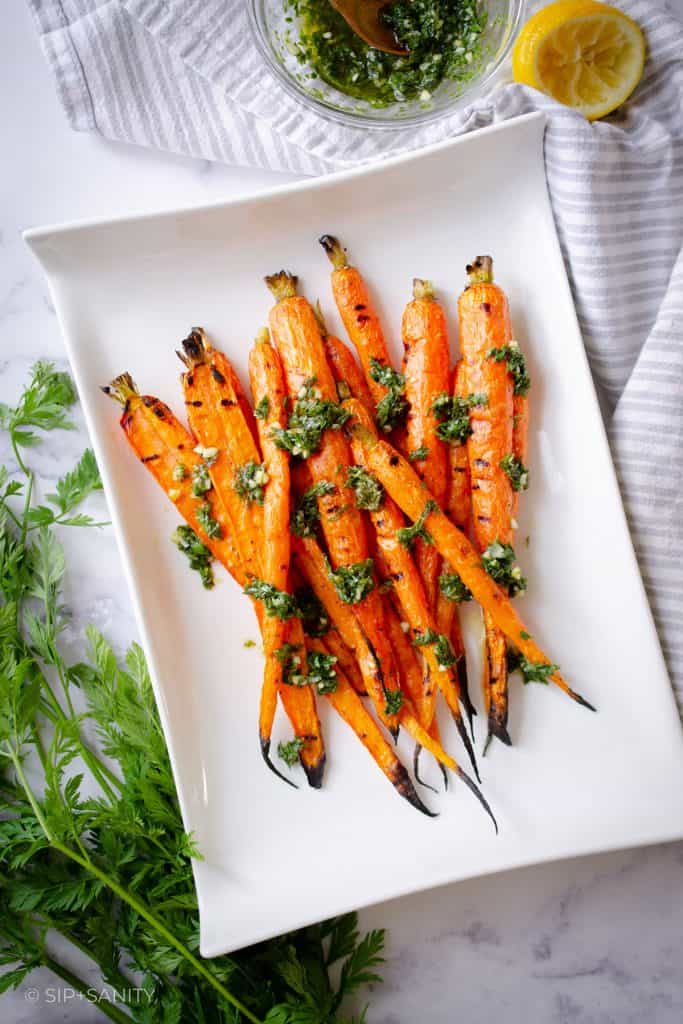 Grilled whole carrots with green herb sauce on a white platter.