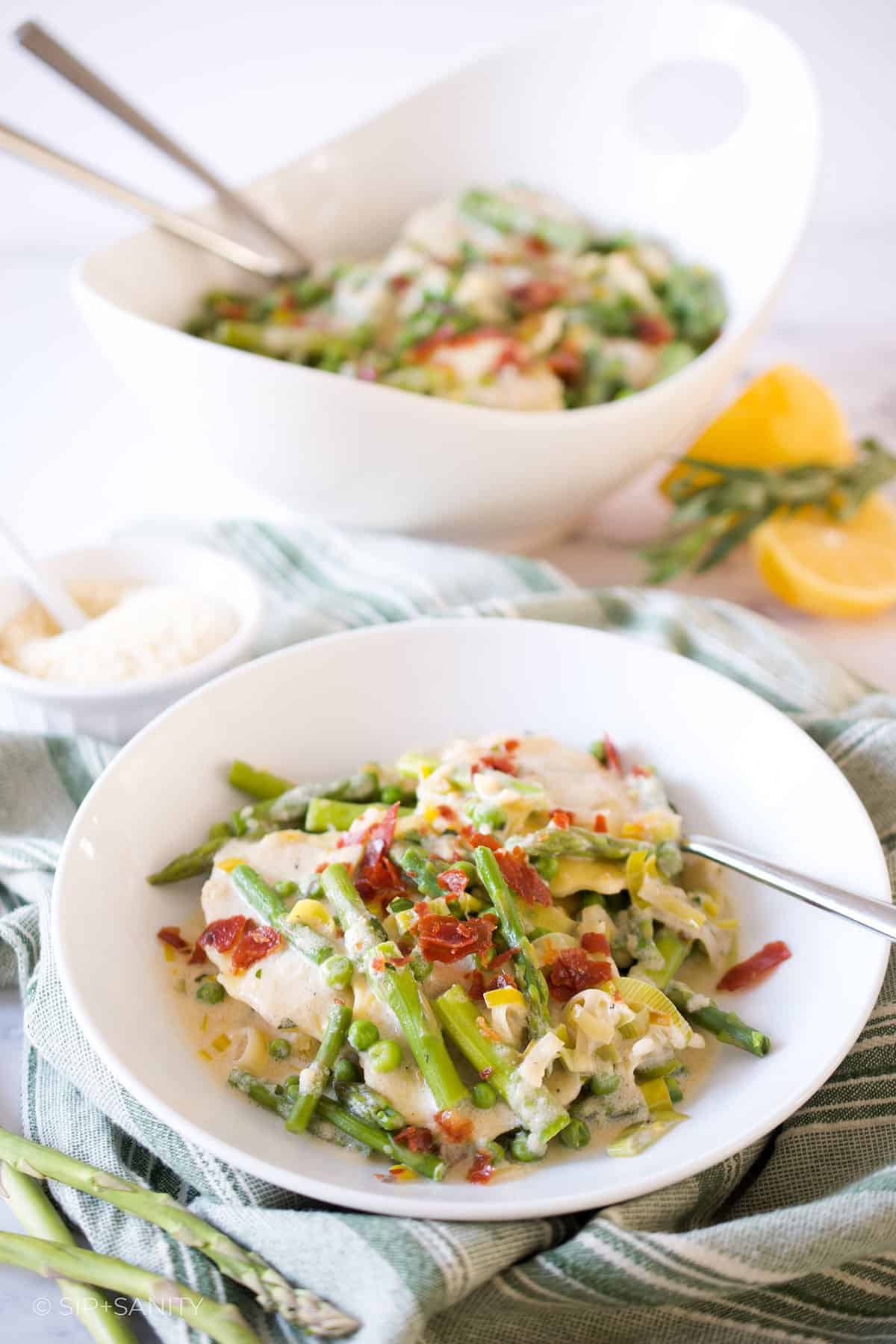 Creamy mushroom ravioli with spring vegetables in a bowl with a fork.