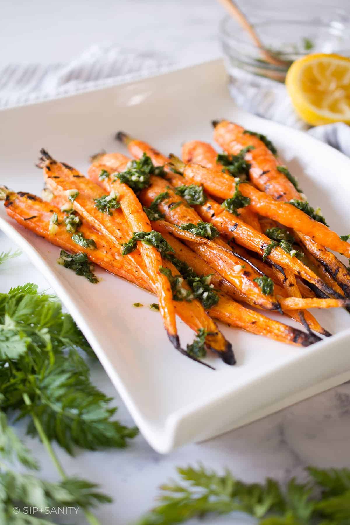 Grilled whole carrots with green herb sauce on a white platter.