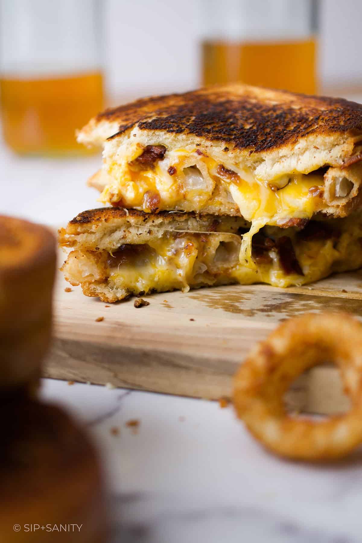 Two halves of an onion ring and bacon grilled cheese sandwich stacked on each other.