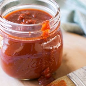 Mason jar full of chipotle honey bbq sauce on a wooden block.