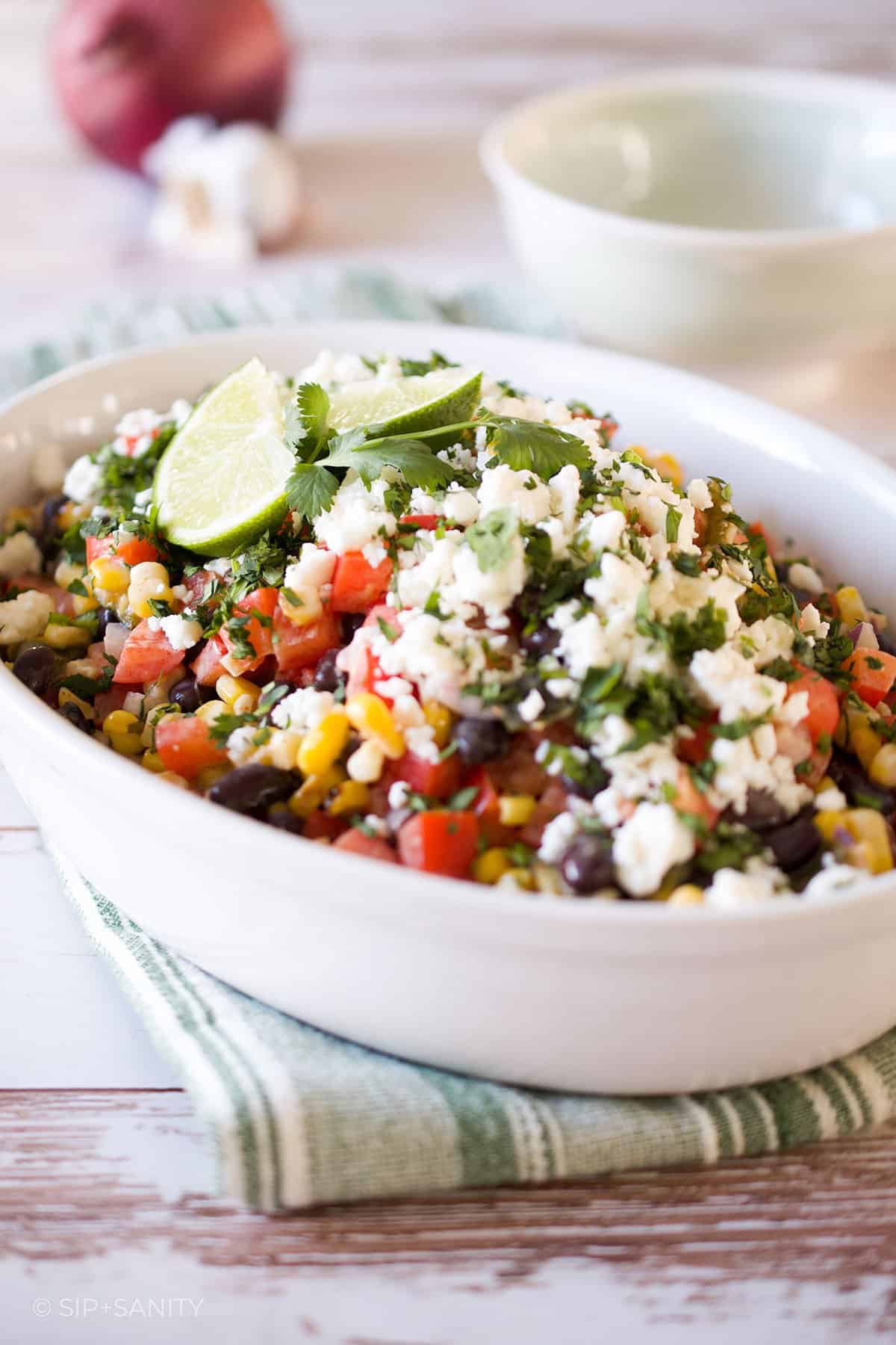 Charred corn salad with black beans in a white dish on a wood table.