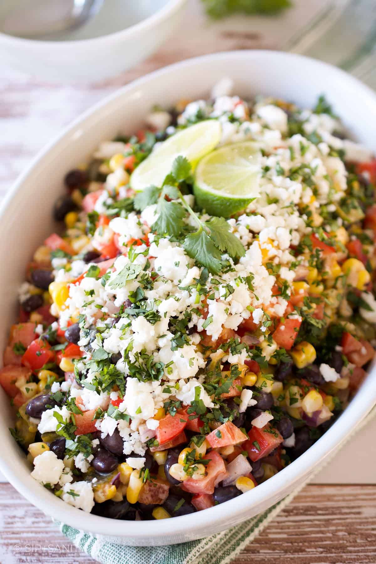 Charred corn salad with black beans in a white dish on a wood table.