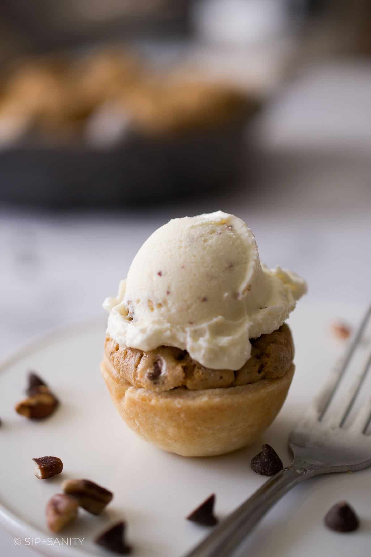 A derby pie tartlet with a tiny scoop of ice cream on top next to a fork.
