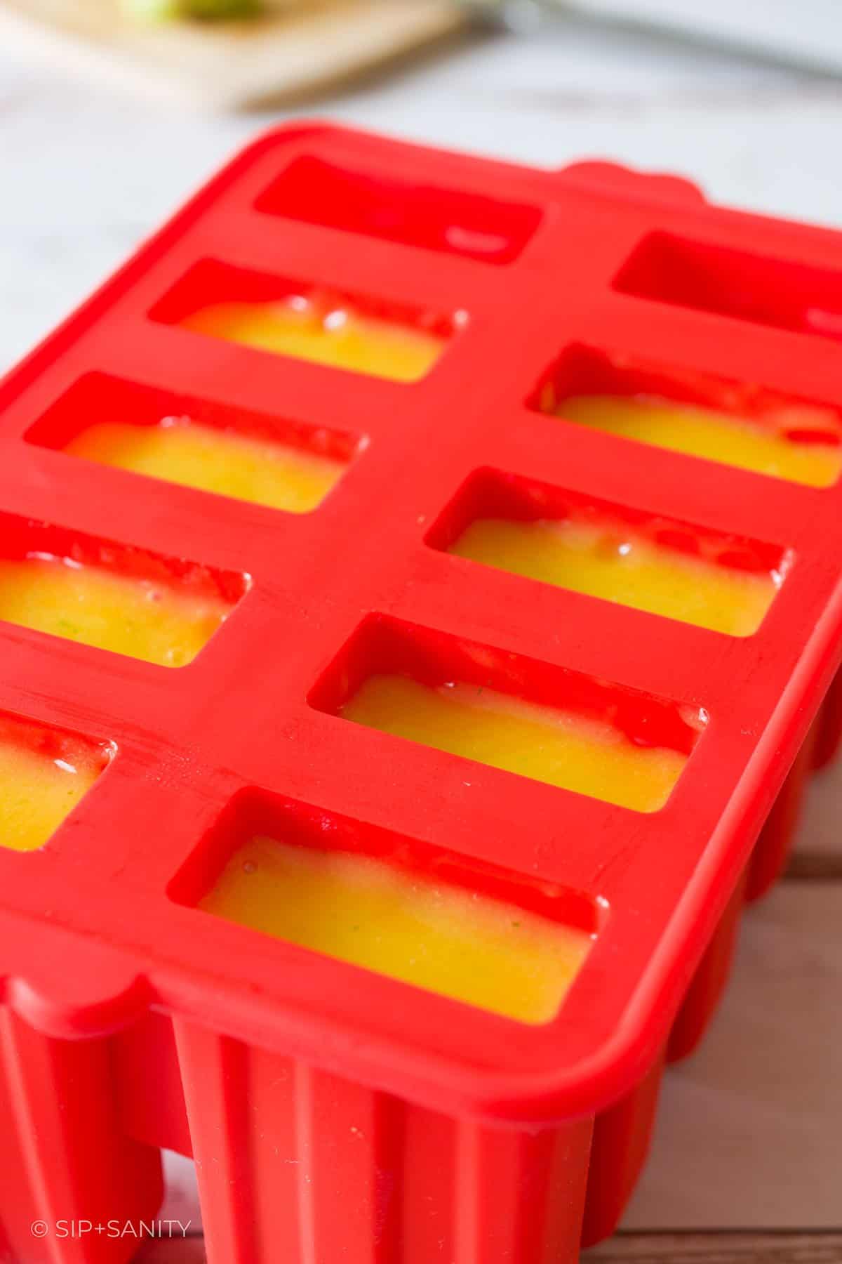 A popsicle mold filled with mango puree.