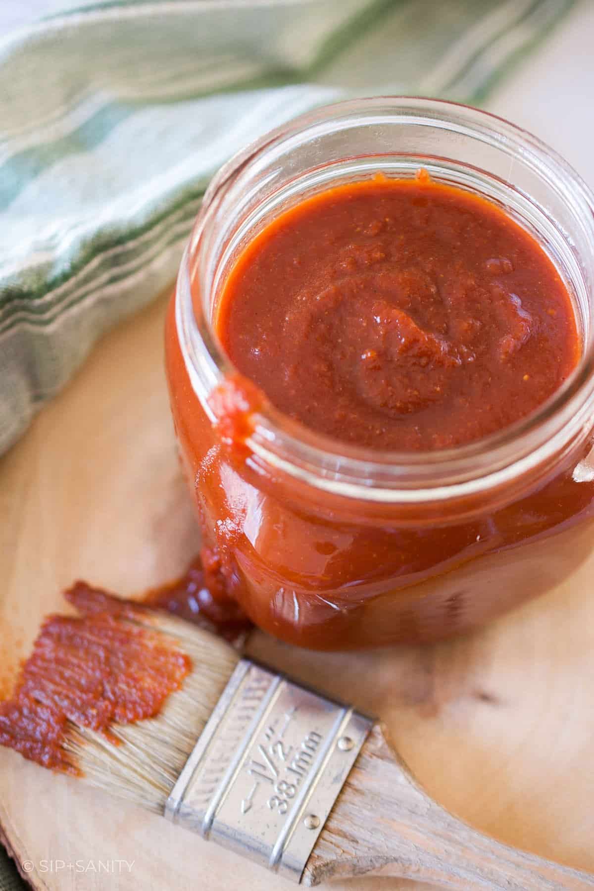 Mason jar full of chipotle honey bbq sauce next to a basting brush.