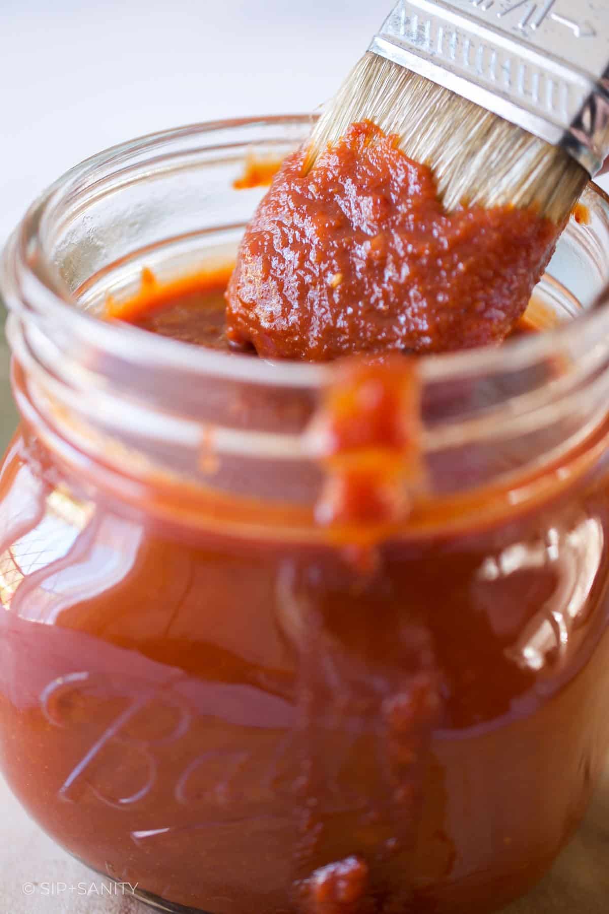 Dipping a basting brush into a jar of bbq sauce.