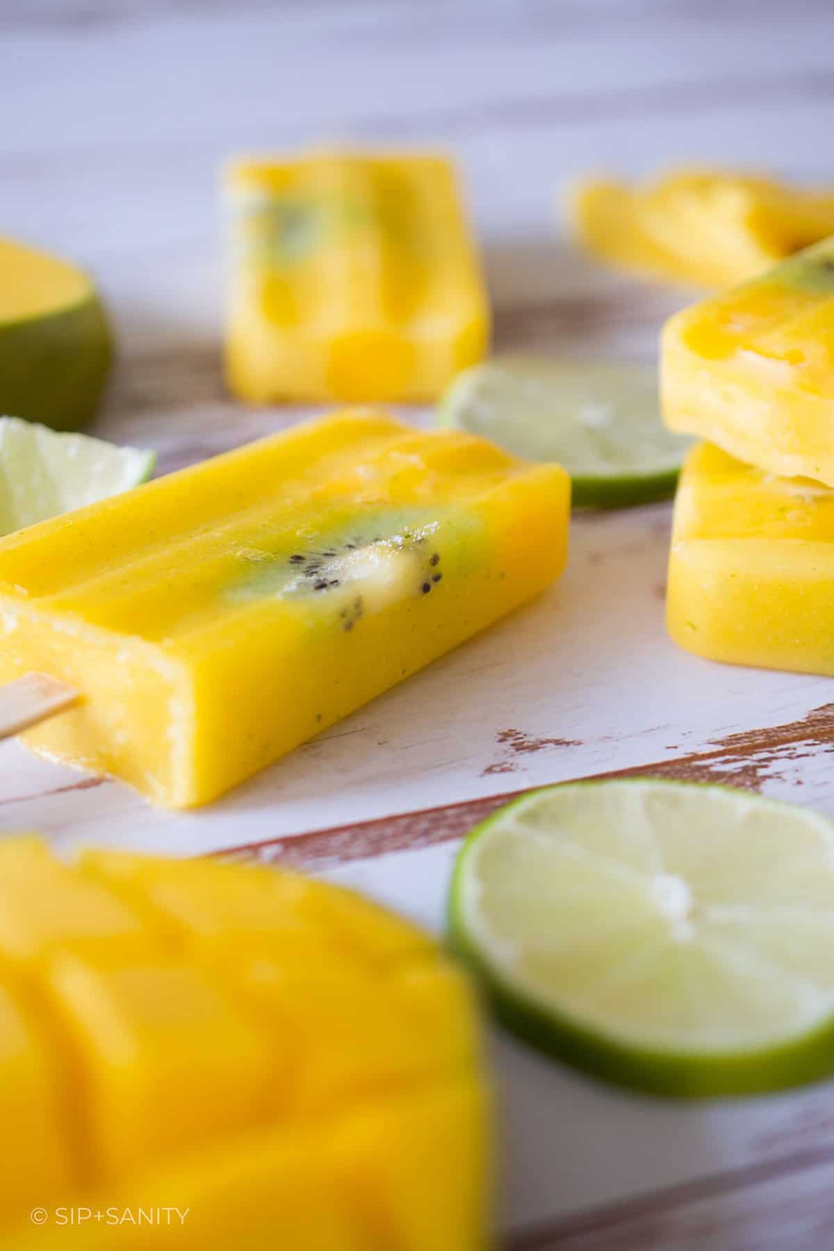 Mango lime popsicles and lime slices on a wooden table.