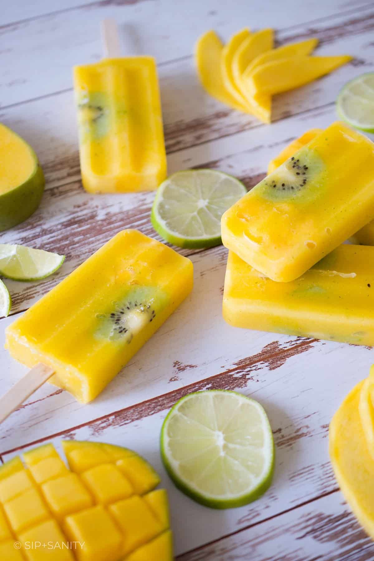 Mango lime popsicles, lime and mango slices on a wooden table.