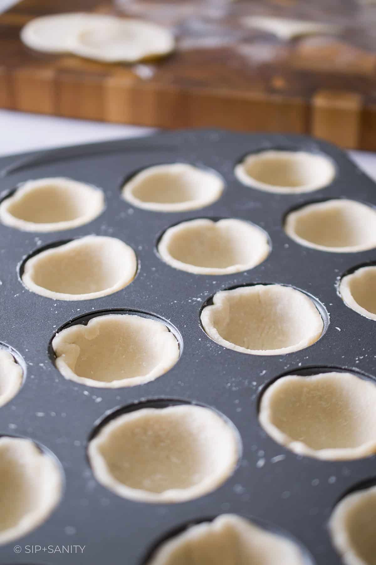 A mini muffin tin filled with small pie shells.