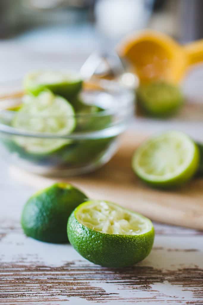 Several halved limes on a white wood table after being juiced.