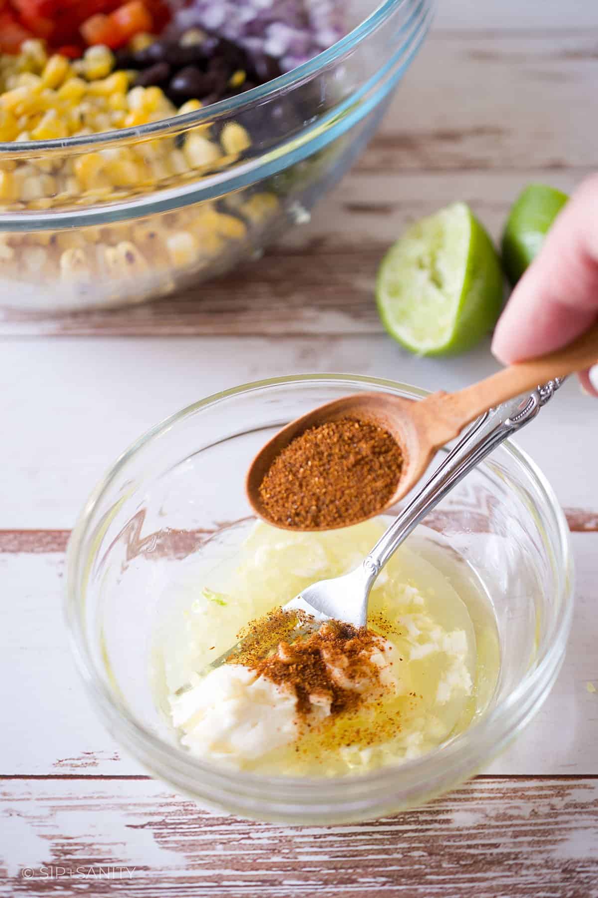 Adding chili powder to creamy lime dressing in a bowl.