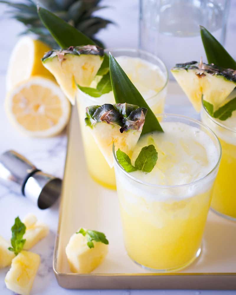 A tray of three glasses of lemonade garnished with pineapple wedges.