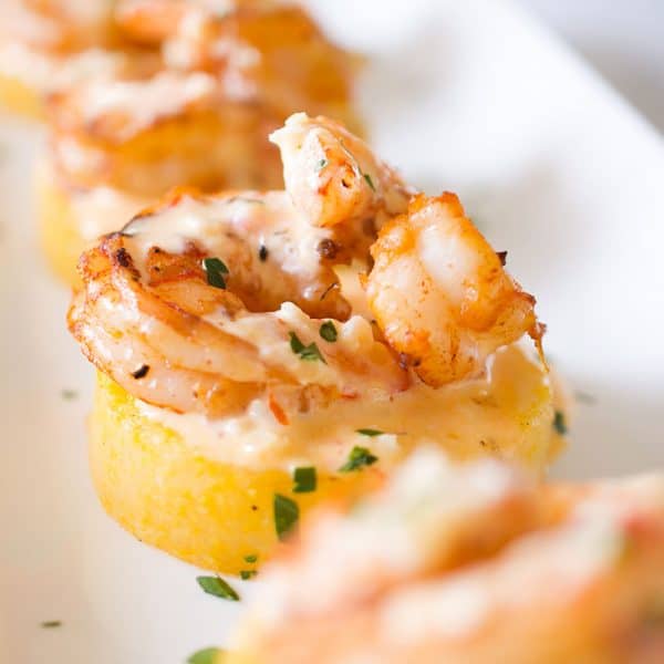 A white platter with four polenta and shrimp appetizers.