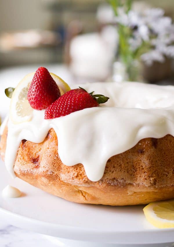 A bundt cake on a platter with white icing and lemons and strawberries on top.