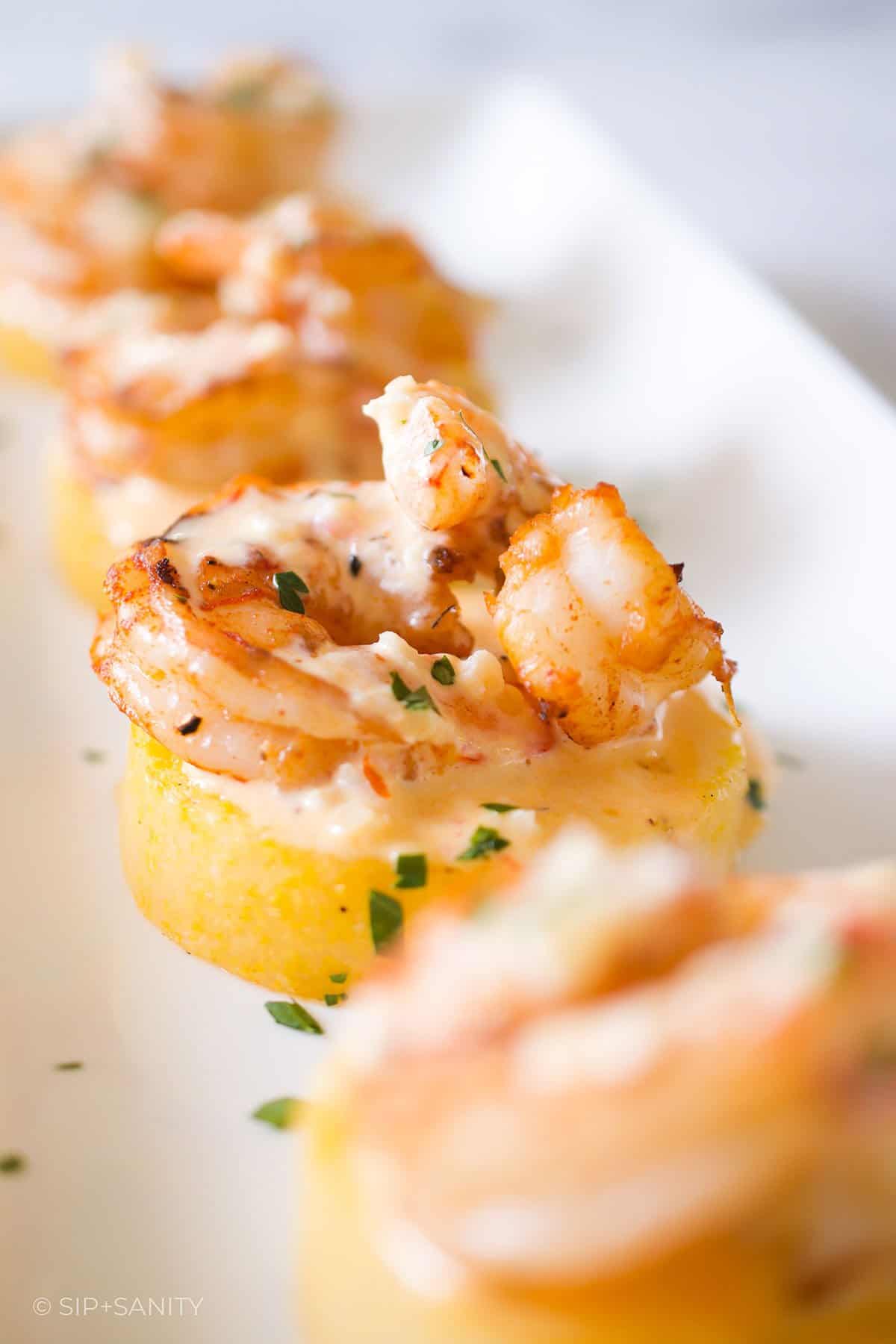 A white platter with four shrimp and polenta appetizers on it.