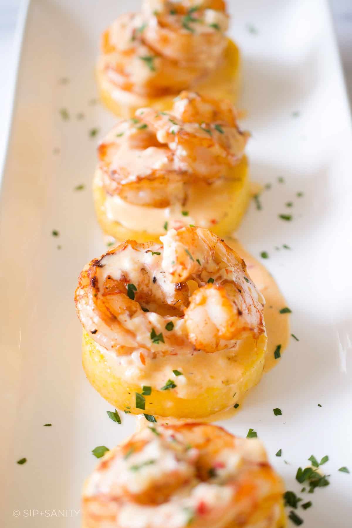 A white platter holding four shrimp and polenta appetizers.