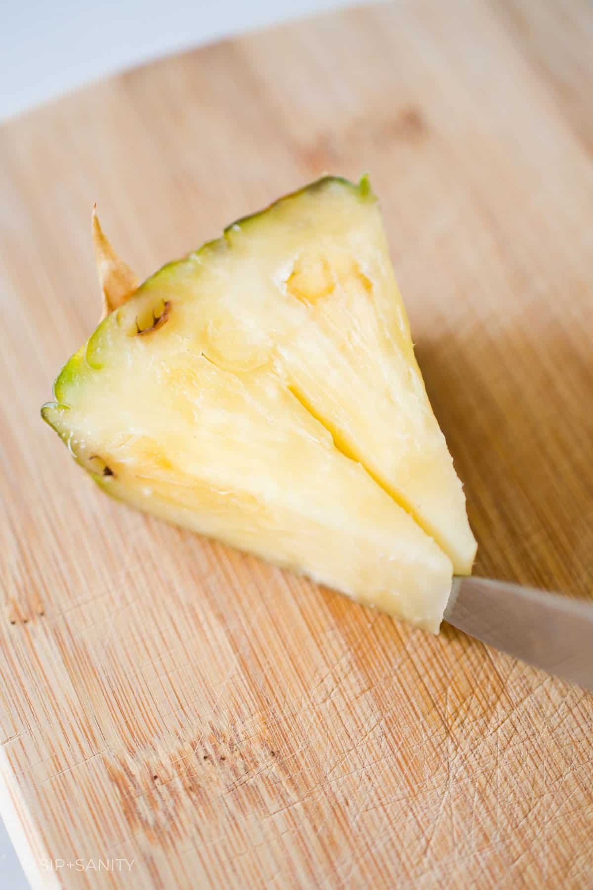 A knife cutting a slit into a wedge of pineapple.