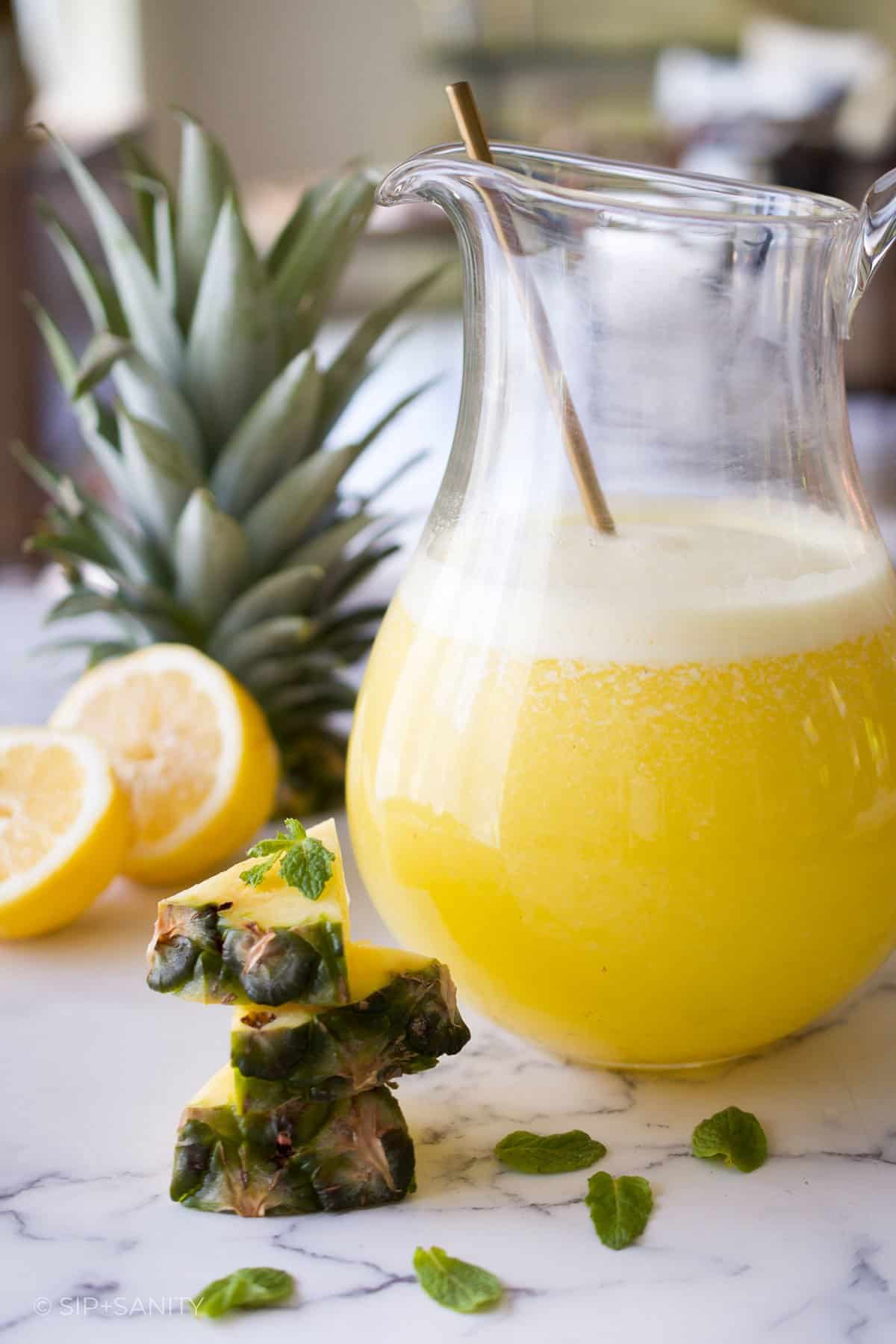 A pitcher of pineapple lemonade next to pineapple wedges and lemons.