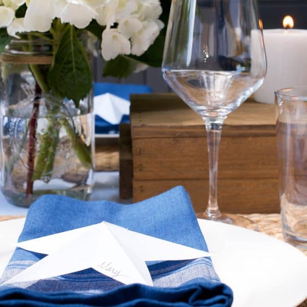 A wine glass, white plate with blue napkin and bouquet of flowers.