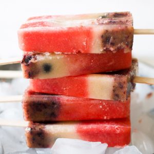 Five red, white and blue popsicles in a stack on a bowl of ice.
