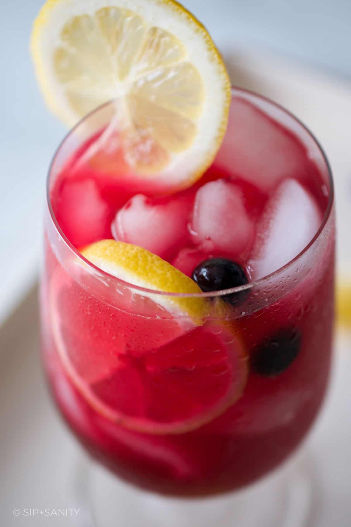 A glass of blueberry hibiscus lemonade garnished with lemon slices.