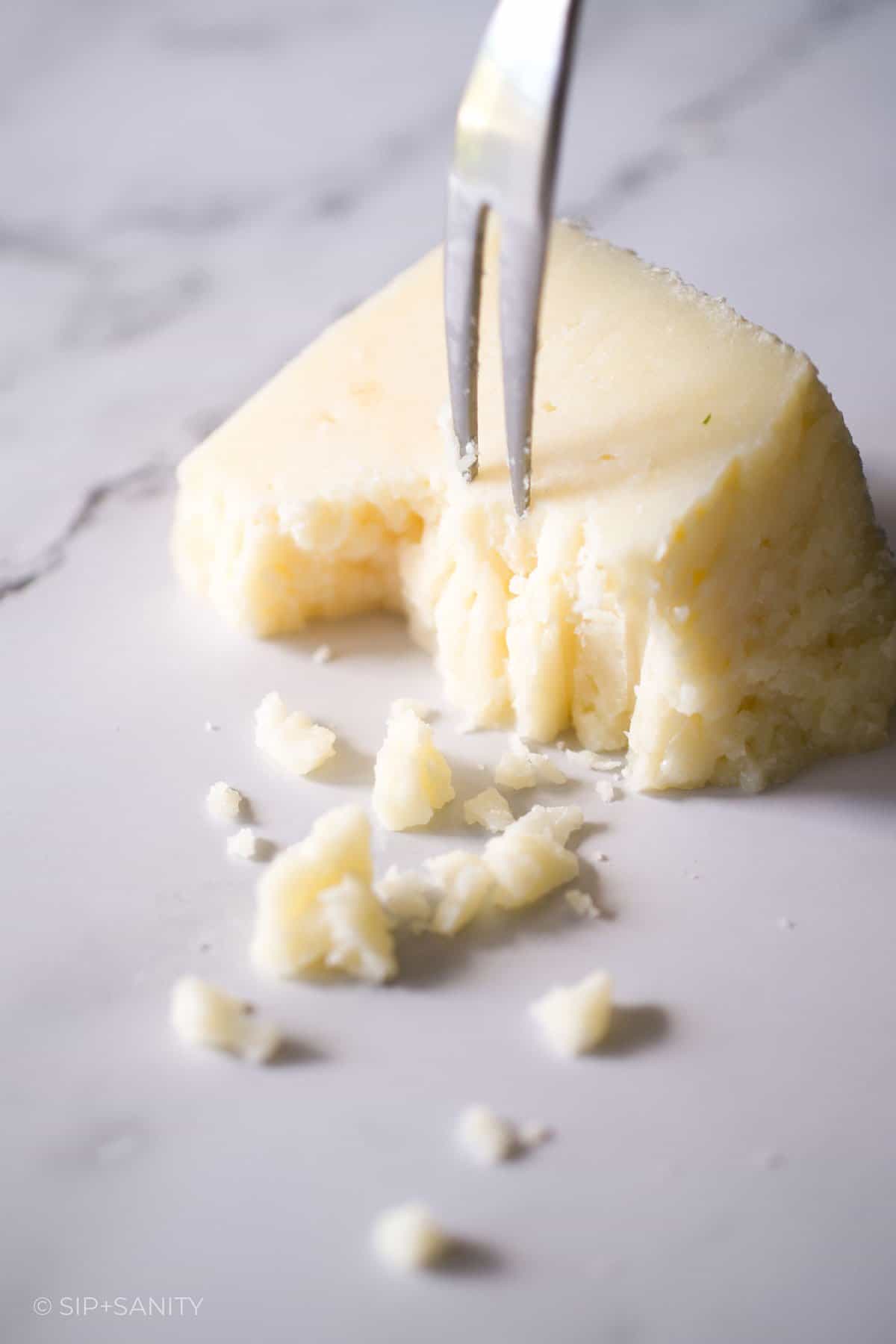 A fork crumbling manchego cheese on a marble counter.