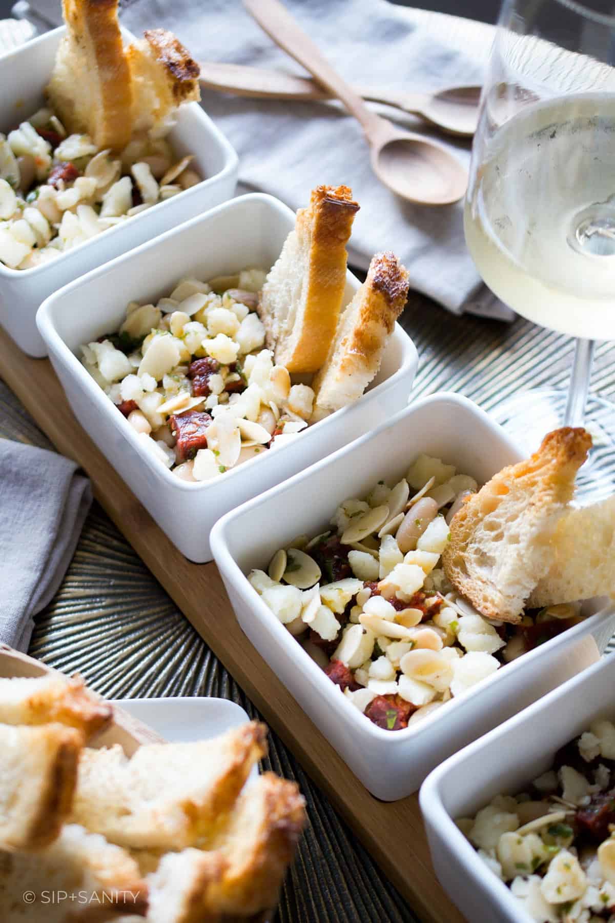 Four servings of white bean salad tapas in square bowls.