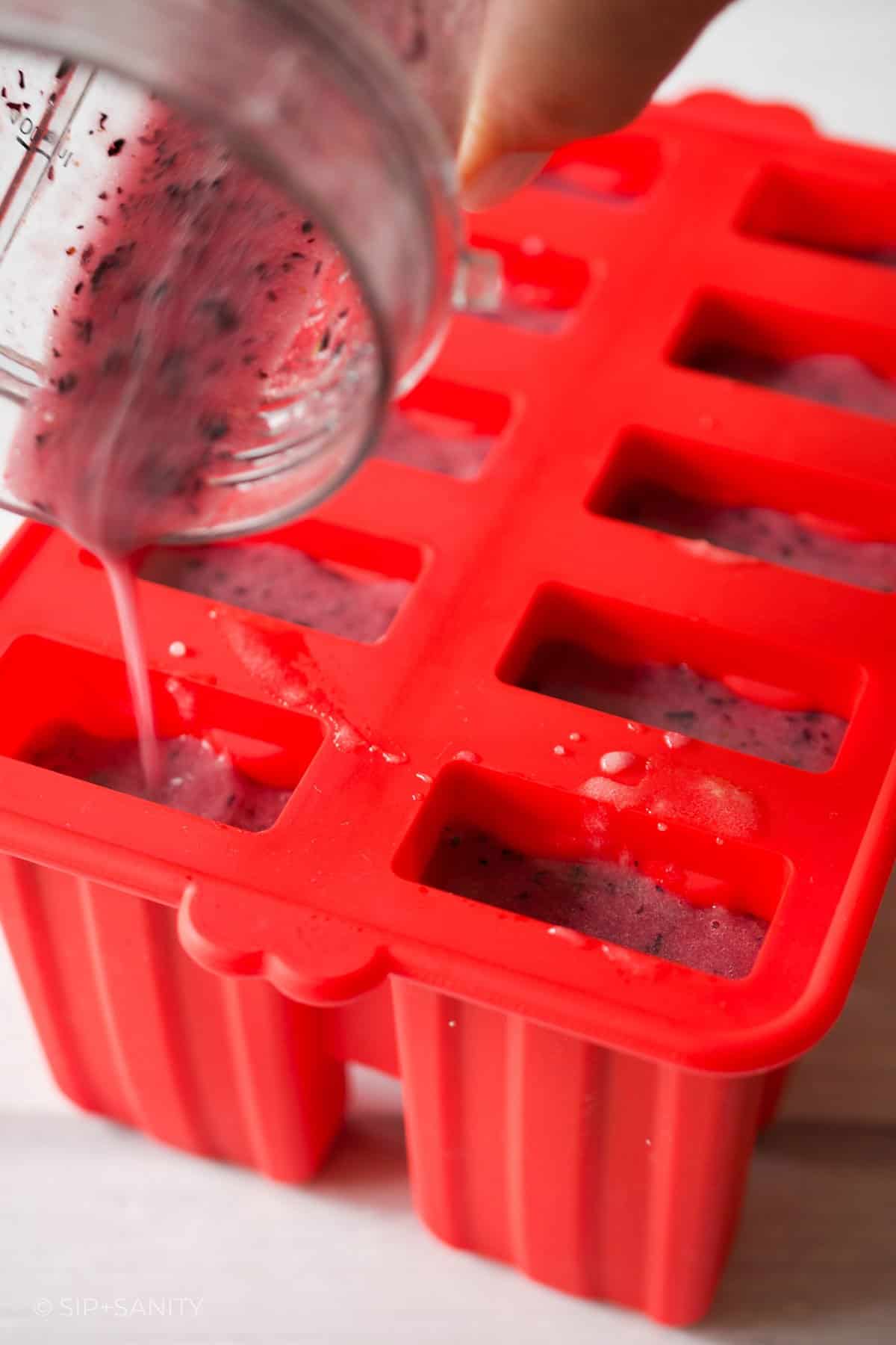 Pouring blueberry puree into popsicle molds.