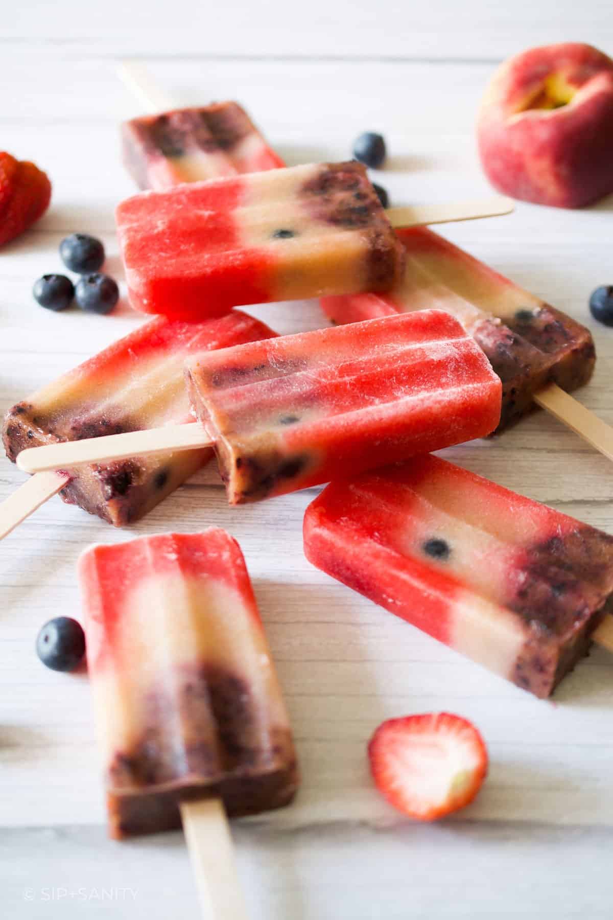 Red, white and blueberry popsicles scattered on a white wooden surface.