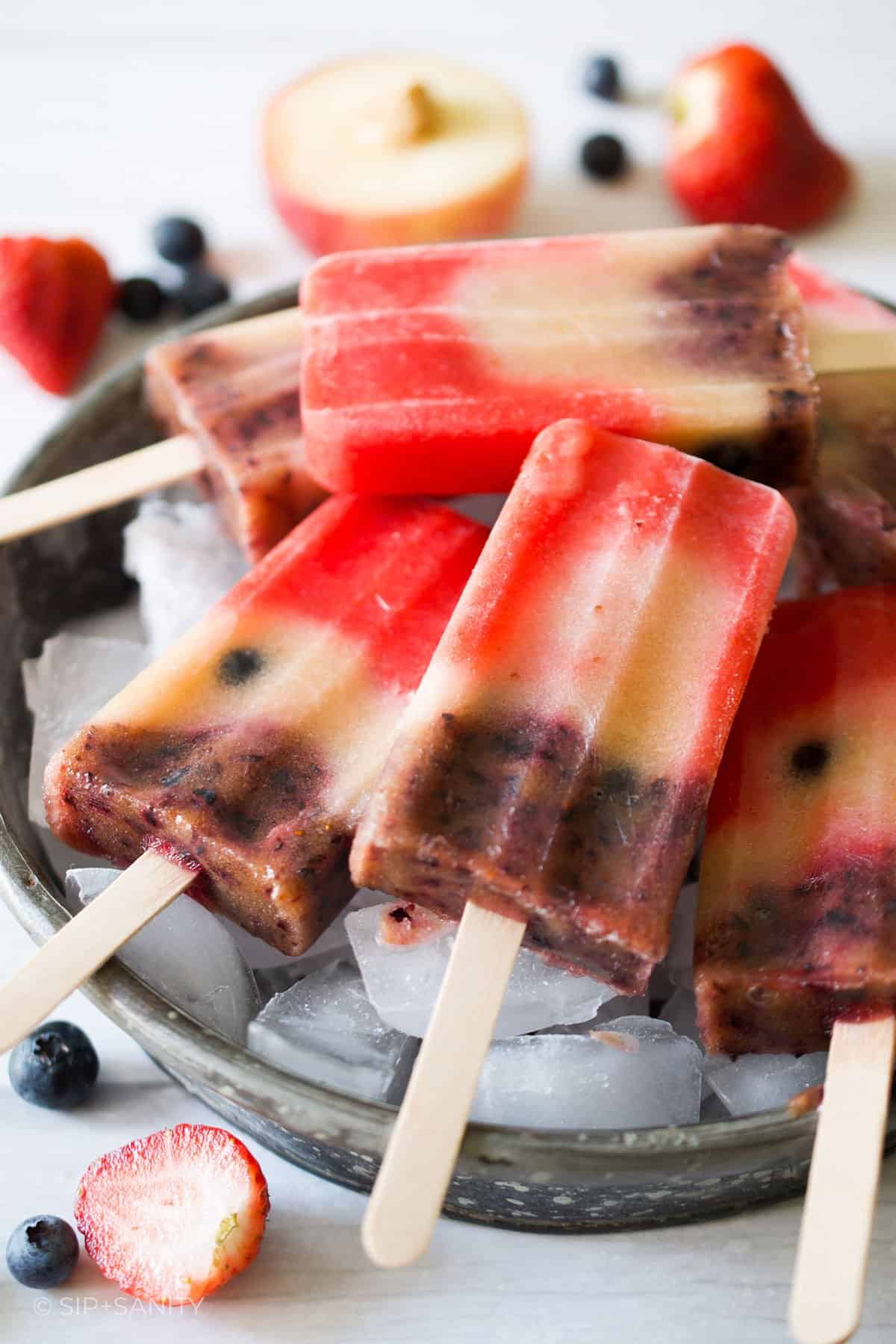 Red, white and blueberry popsicles resting in a tin bowl full of ice.