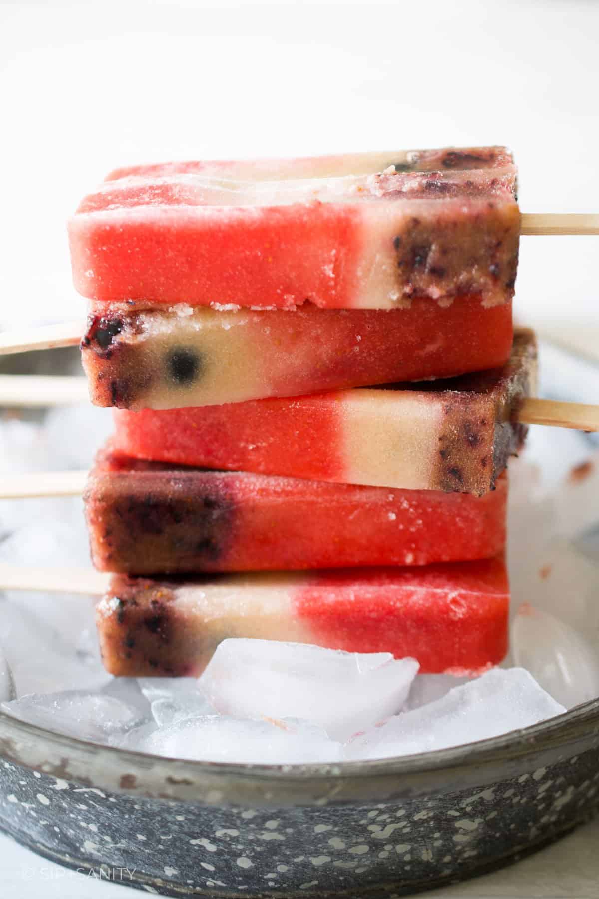 Five red, white and blue popsicles in a stack on a bowl of ice.