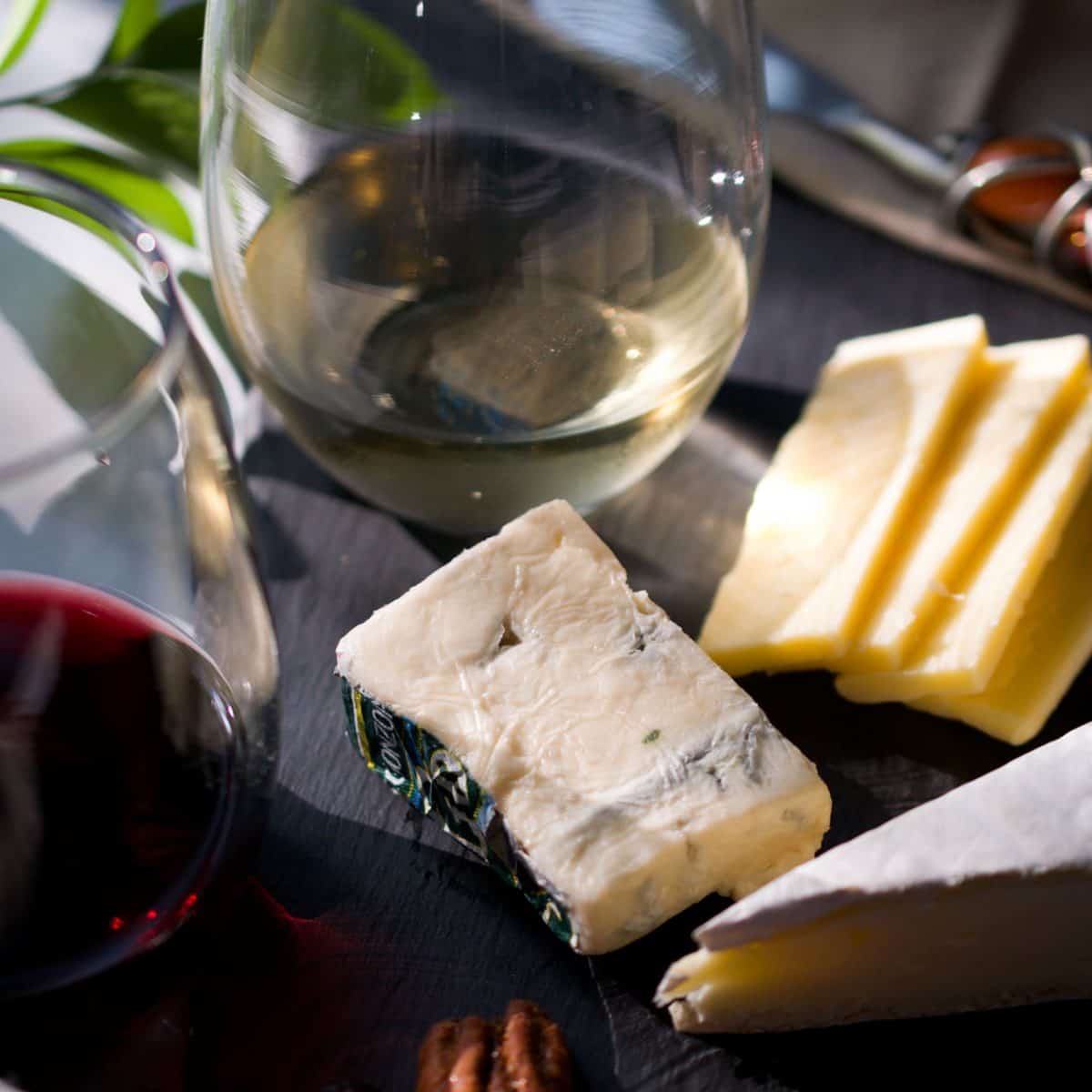 Two glasses of wine and some cheeses on a slate board.