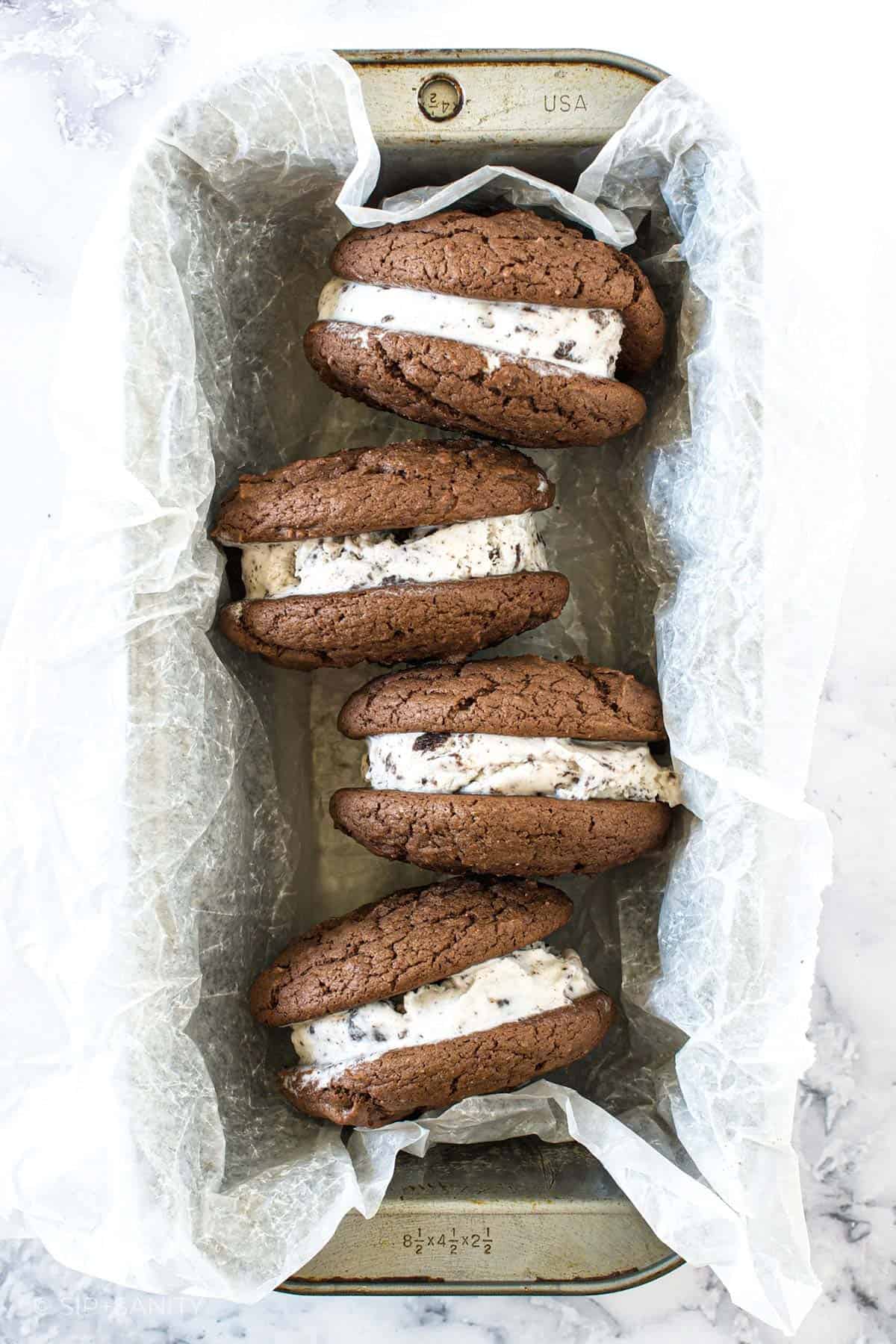 Four cookie ice cream sandwiches in a wax paper lined tin.