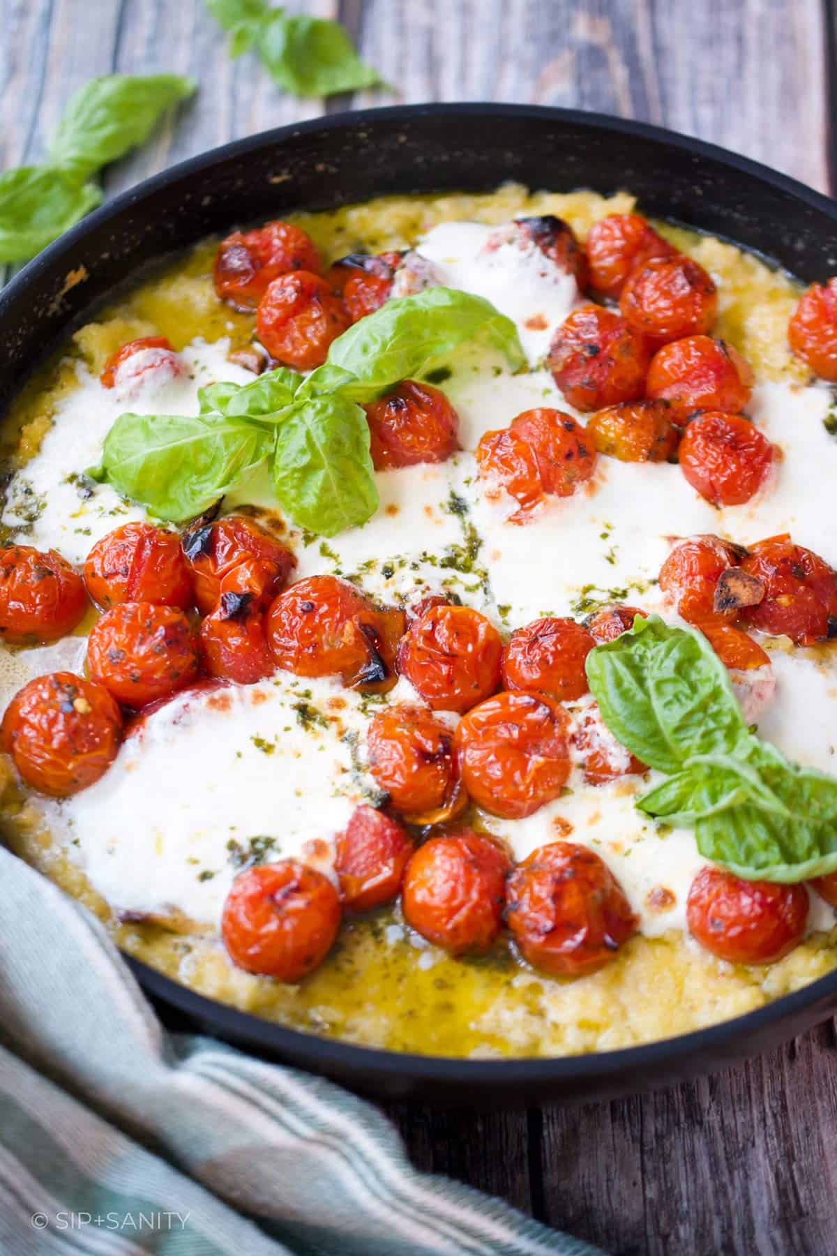 A skillet of polenta, tomatoes and burrata on a wooden table.
